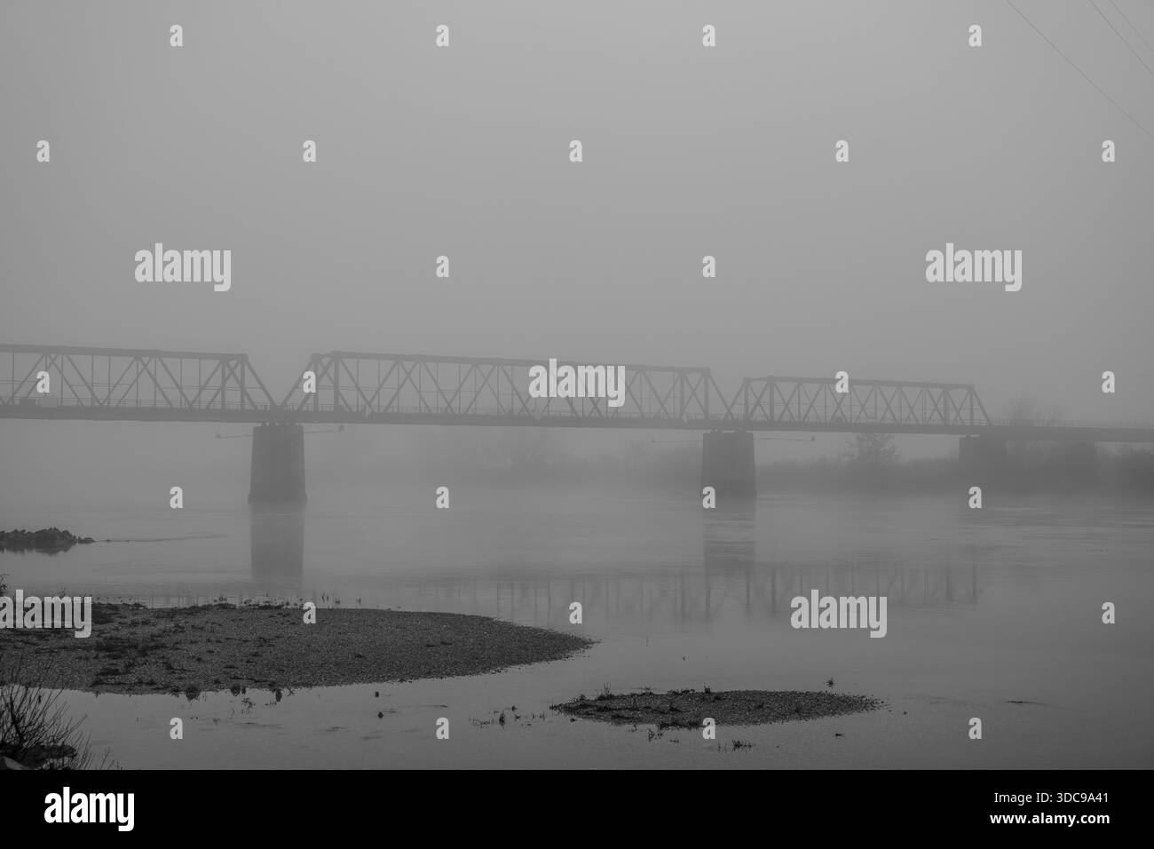 Die Eisenbahnbrücke über die Donau steht noch im Nebel. Das Wasser reflektiert die Struktur. Der Tag endet mit dicken Wolken und geringer Sicht. Bogen, Unten Stockfoto