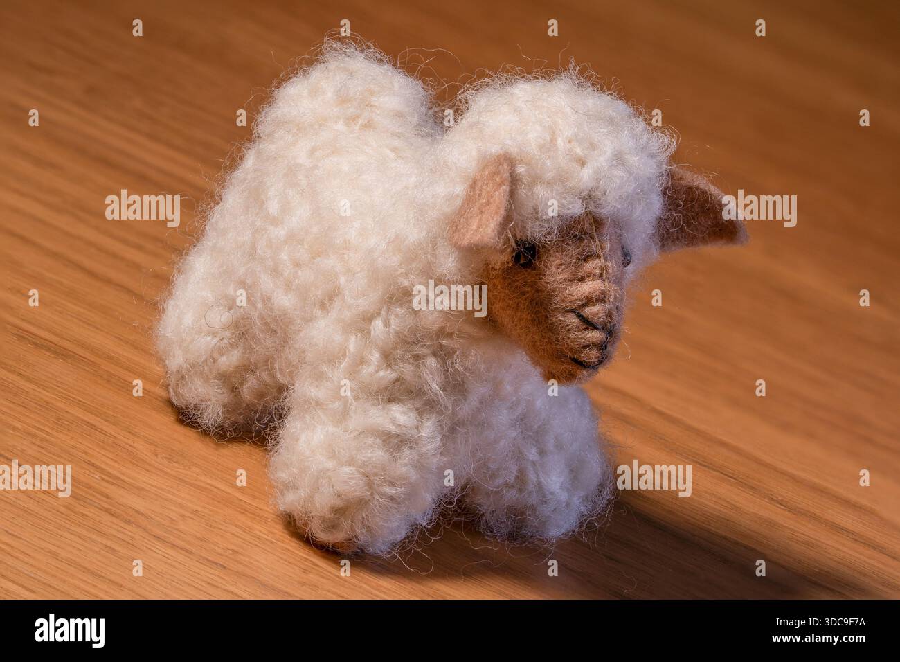 Ein flauschiges weißes Plüschtier in Schafform mit detailliertem braunem Gesicht und Ohren sitzt auf einer polierten Holzoberfläche. Stockfoto