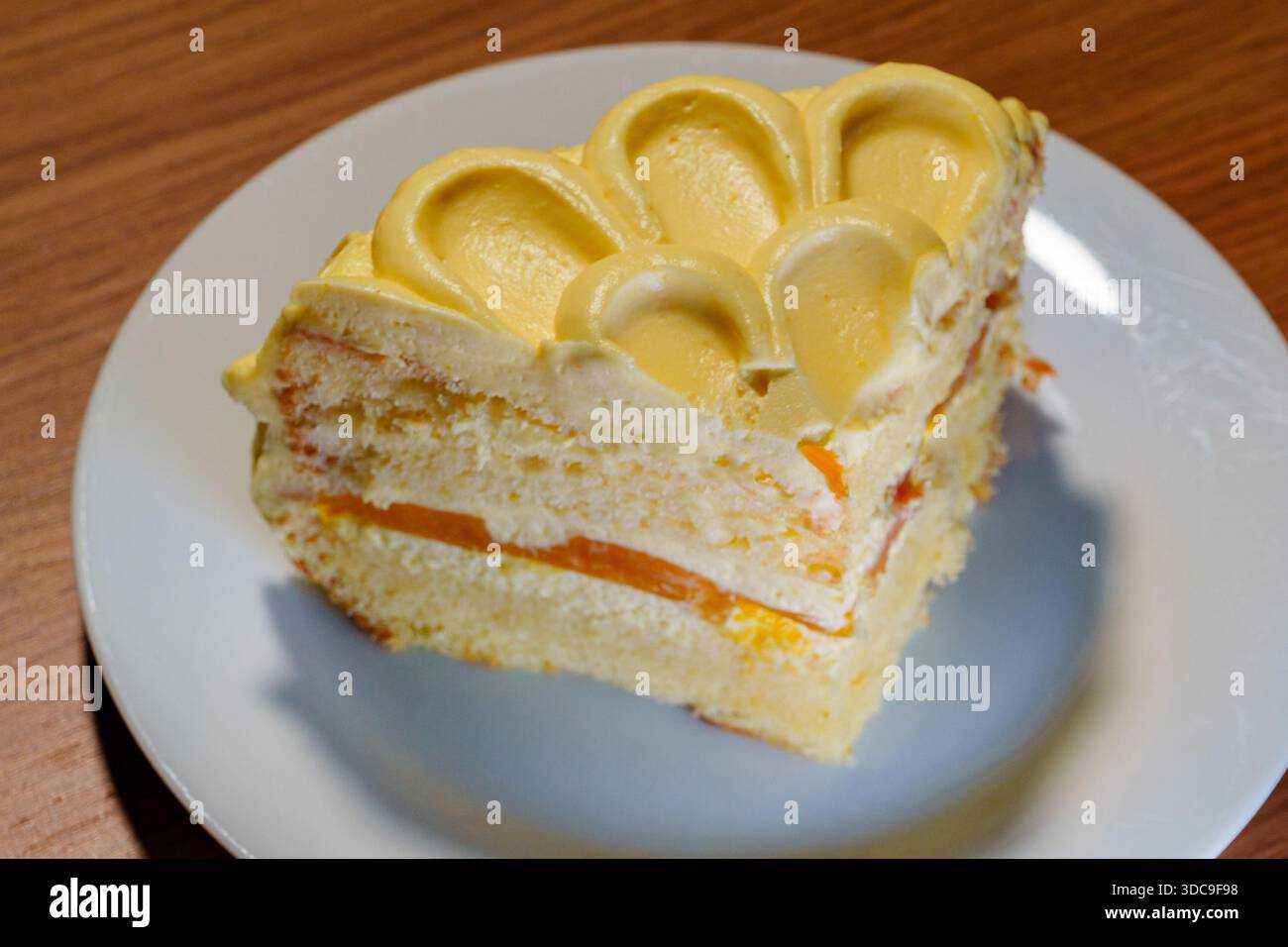 Eine dreieckige Scheibe Vanilleschwammkuchen mit cremeweißen Schichten und Orangenkompott, gekrönt mit gelbem Zuckerguss. Stockfoto