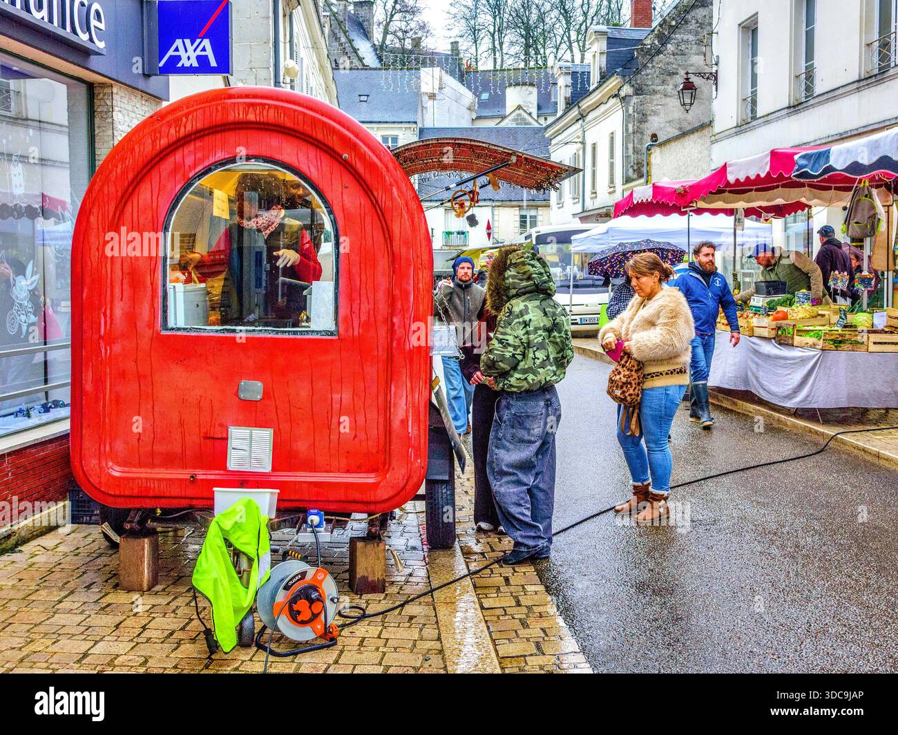 Kunden, die an regnerischem Tag auf dem Markt unter freiem Himmel warmes Essen aus einem kleinen Wohnwagen in Loches, Indre-et-Loire (37), Frankreich anstehen. Stockfoto