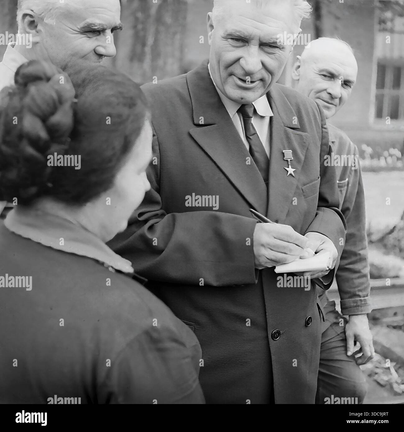 Slaviansk, Ukrainische SSR, UdSSR - 1981: Archivfoto eines Helden der Sozialistischen Arbeiterbewegung, der mit Eisenbahnarbeitern zusammentrefft. Der ältere Deputy, der einen formellen Anzug und die Goldstern-Medaille trägt, schreibt fleißig Notizen in einem Block, während er einer Frau und einem Mann in Arbeitskleidung zuhört. Die Gruppe steht in der Nähe von Bahngleisen. Dieses Bild erfasst die Interaktion zwischen der lokalen Elite und der Arbeiterklasse und unterstreicht die Reaktionsfähigkeit der Regierung in der friedlichen Donbass-Region während der späten Sowjetzeit. Stockfoto