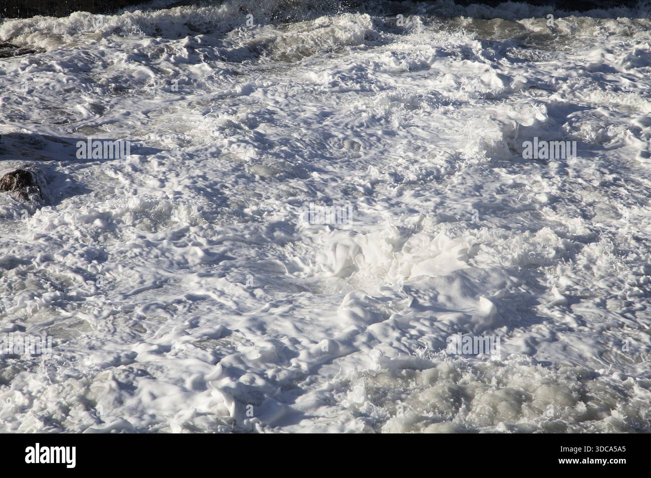 Wellen schaumen heftig auf, wenn sie unter grauem Himmel mit der Küste kollidieren. Stockfoto
