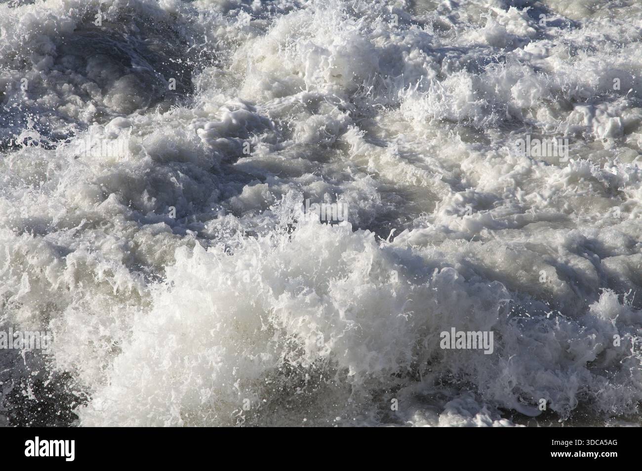 Wellen schaumen heftig auf, wenn sie unter grauem Himmel mit der Küste kollidieren. Stockfoto