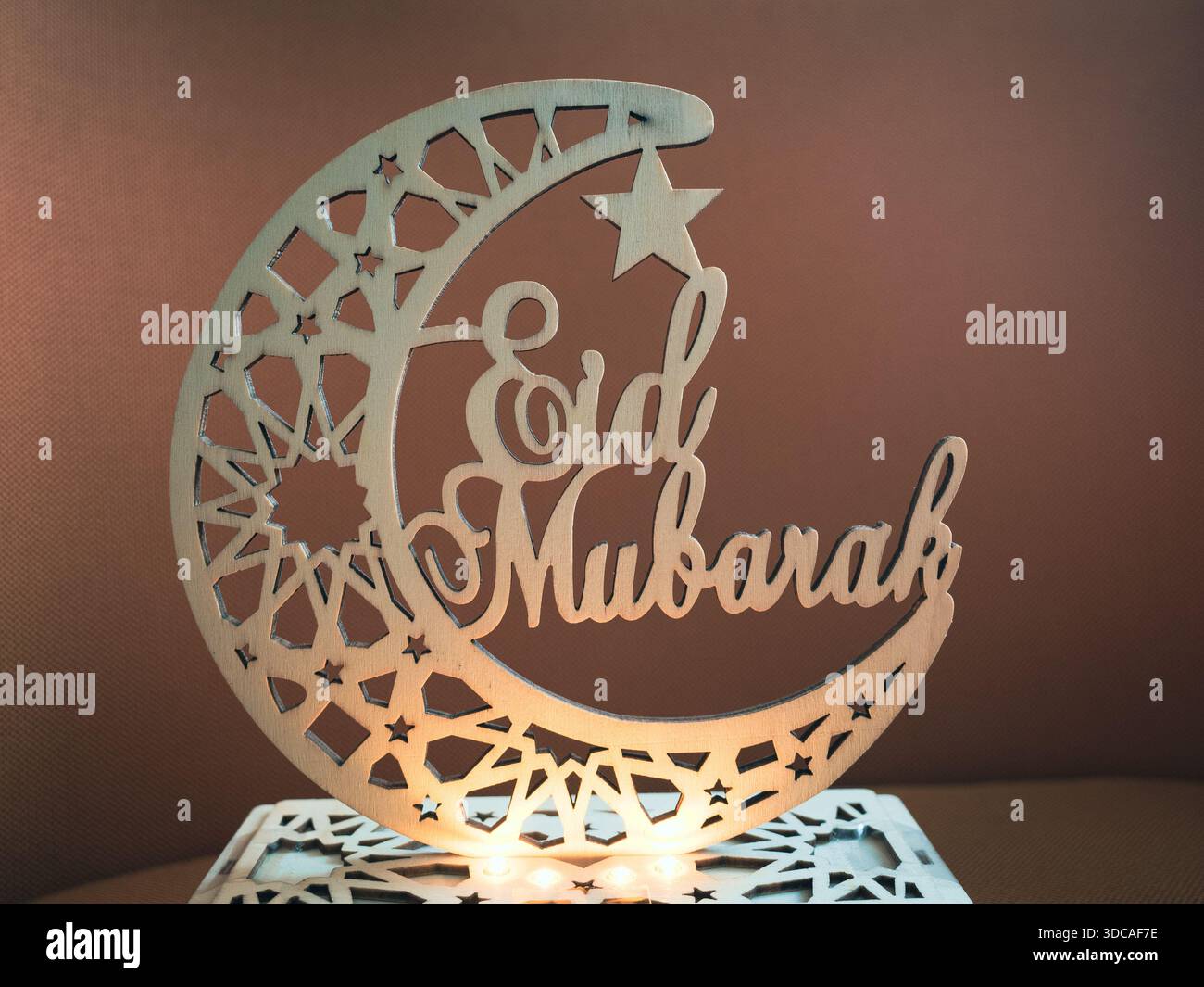 Elegantes hölzernes Eid Mubarak-Ornament mit Mondsichel und Stern mit geometrischen Mustern und warmen leuchtenden Lichtern. Stockfoto