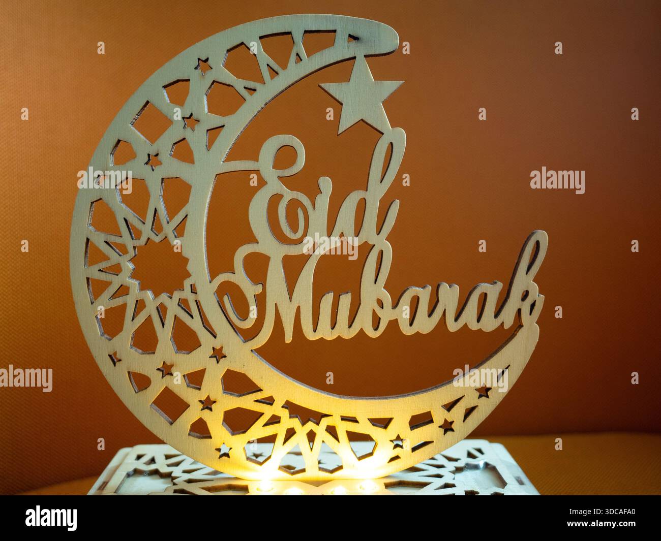 Elegantes hölzernes Eid Mubarak-Ornament mit Mondsichel und Stern mit geometrischen Mustern und warmen leuchtenden Lichtern. Stockfoto