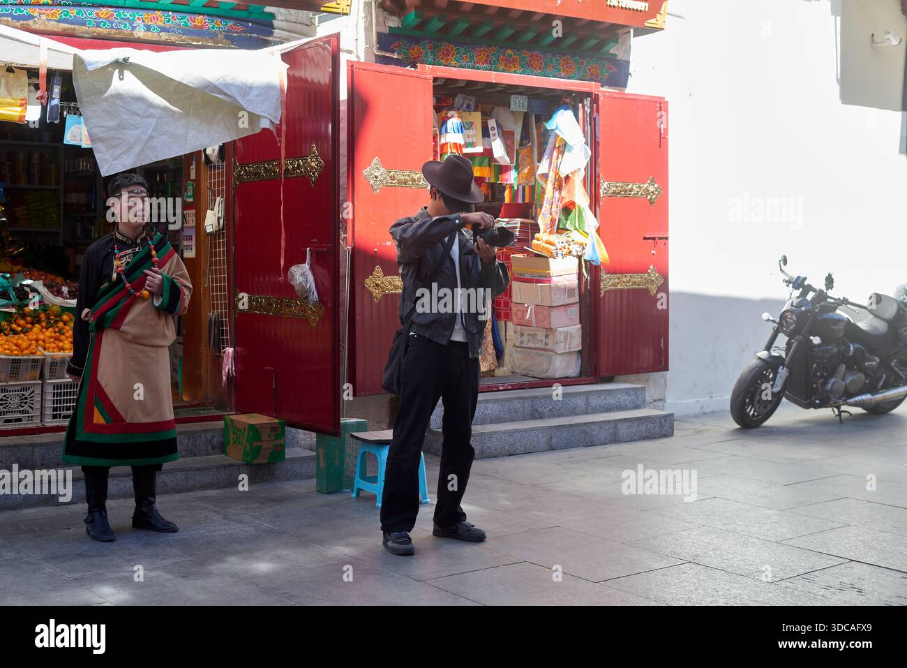 Oktober 2025. Lhasa, Tibet. Person in traditioneller Kleidung und Mann mit Kamera auf der Lhasa Street Stockfoto