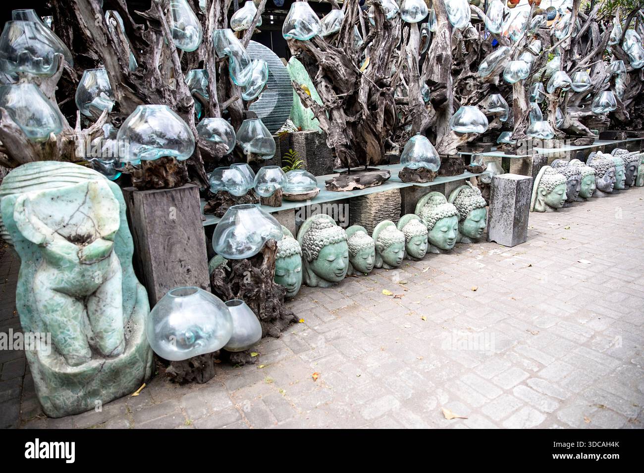 Indonesische Schüsseln aus geschmolzenem Glas auf Treibholzbasis und Buddha-Statuen aus Stein auf einem lokalen Kunsthandwerksmarkt in Indonesien. Stockfoto