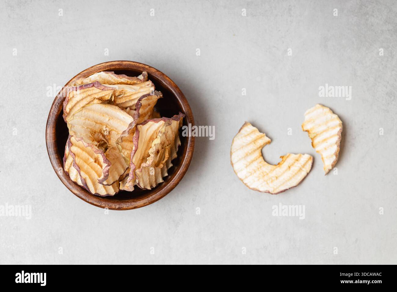 Apfelchips in einer Holzschale auf hellgrauem Hintergrund. Ein gesunder und köstlicher Snack voller Vitamine. Geeignet für Vegetarier. Stockfoto