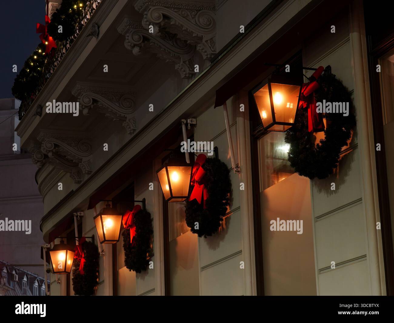 Weihnachtsdekoration mit leuchtenden Laternen und Tannenkränzen an der Fassade des Gebäudes im Zentrum von Bukarest bei Nacht Stockfoto