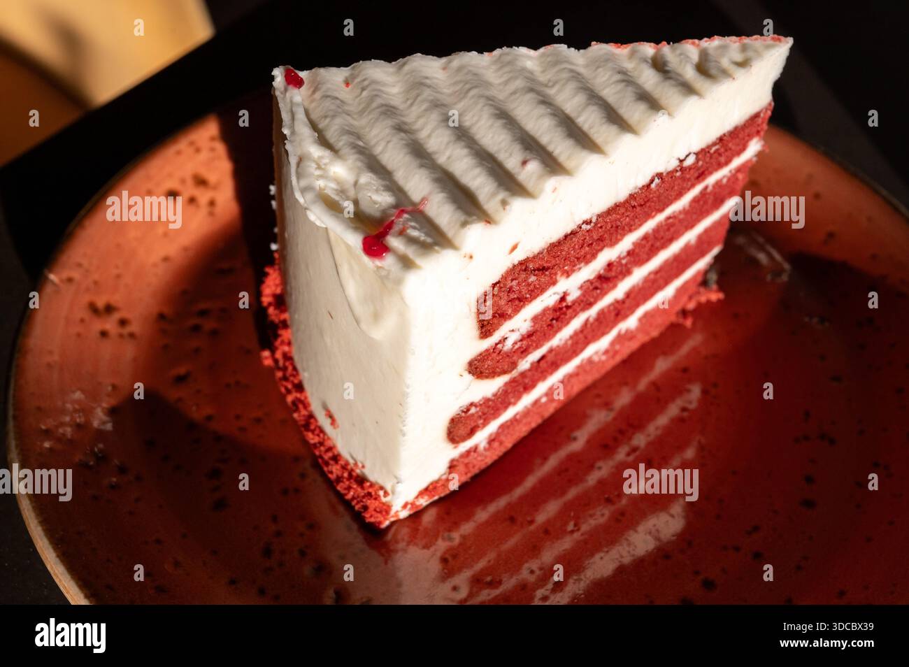 Mehrschichtiger Tortenkuchen mit weißen Cremeschichten und rotem Biskuit mit Beeren, serviert auf einem stilvollen roten Teller in Marsaxlokk, Malta, 6. Dezember 2025. Stockfoto