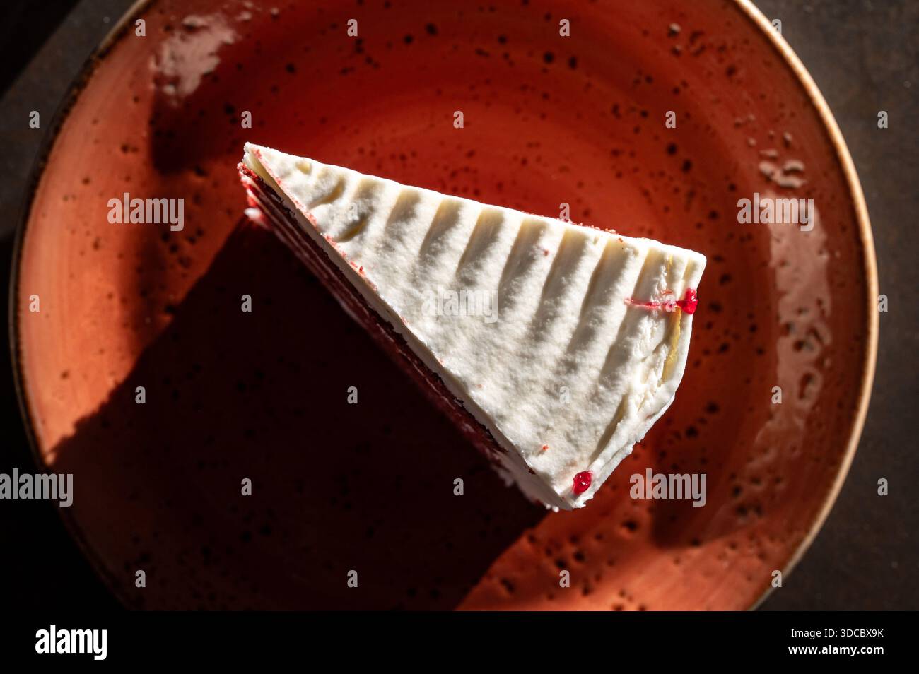 Mehrschichtiger Tortenkuchen mit weißen Cremeschichten und rotem Biskuit mit Beeren, serviert auf einem stilvollen roten Teller in Marsaxlokk, Malta, 6. Dezember 2025. Stockfoto