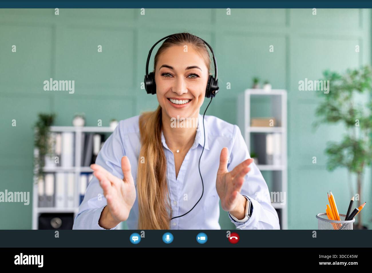 Eine fröhliche Frau mit Kopfhörern lächelt, während sie an einem Videoanruf aus ihrem Heimbüro teilnimmt. Sie setzt sich mit ihrer Webcam auseinander und zeigt Enthusiasmus A Stockfoto
