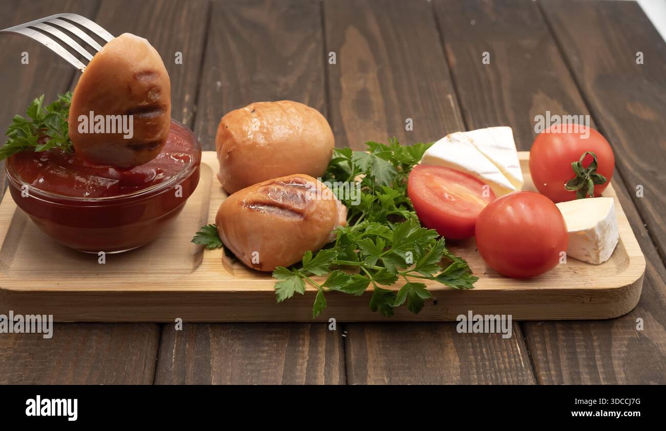 Gegrillte Würstchen mit Tomaten, Käse und Ketchup auf hölzernem Servierbrett, rustikale hausgemachte Speisen Stockfoto