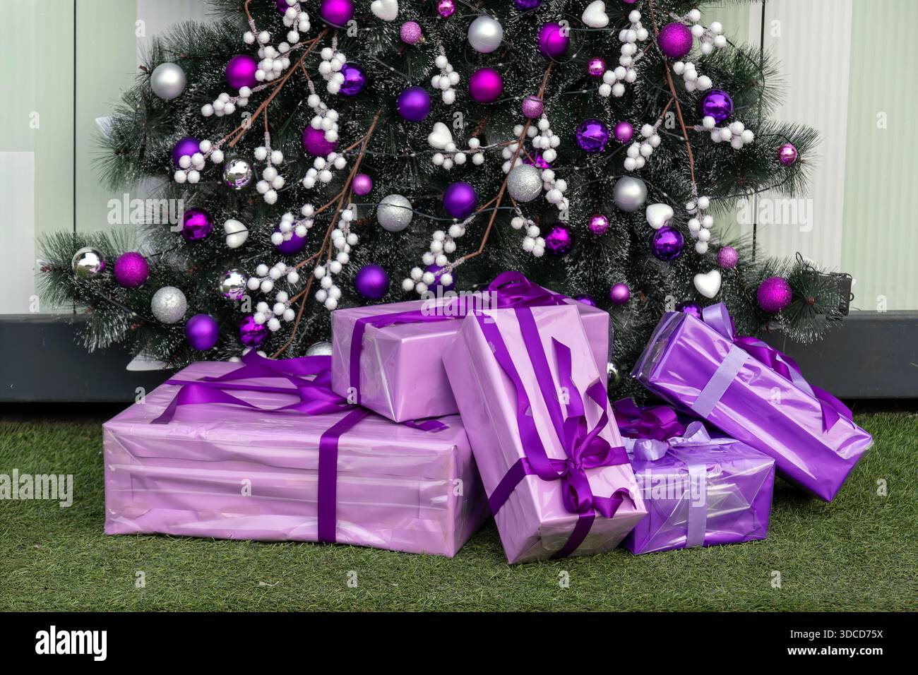 Weihnachtsbaumdetail mit lila Ornamenten und Geschenkartikeln darunter Stockfoto