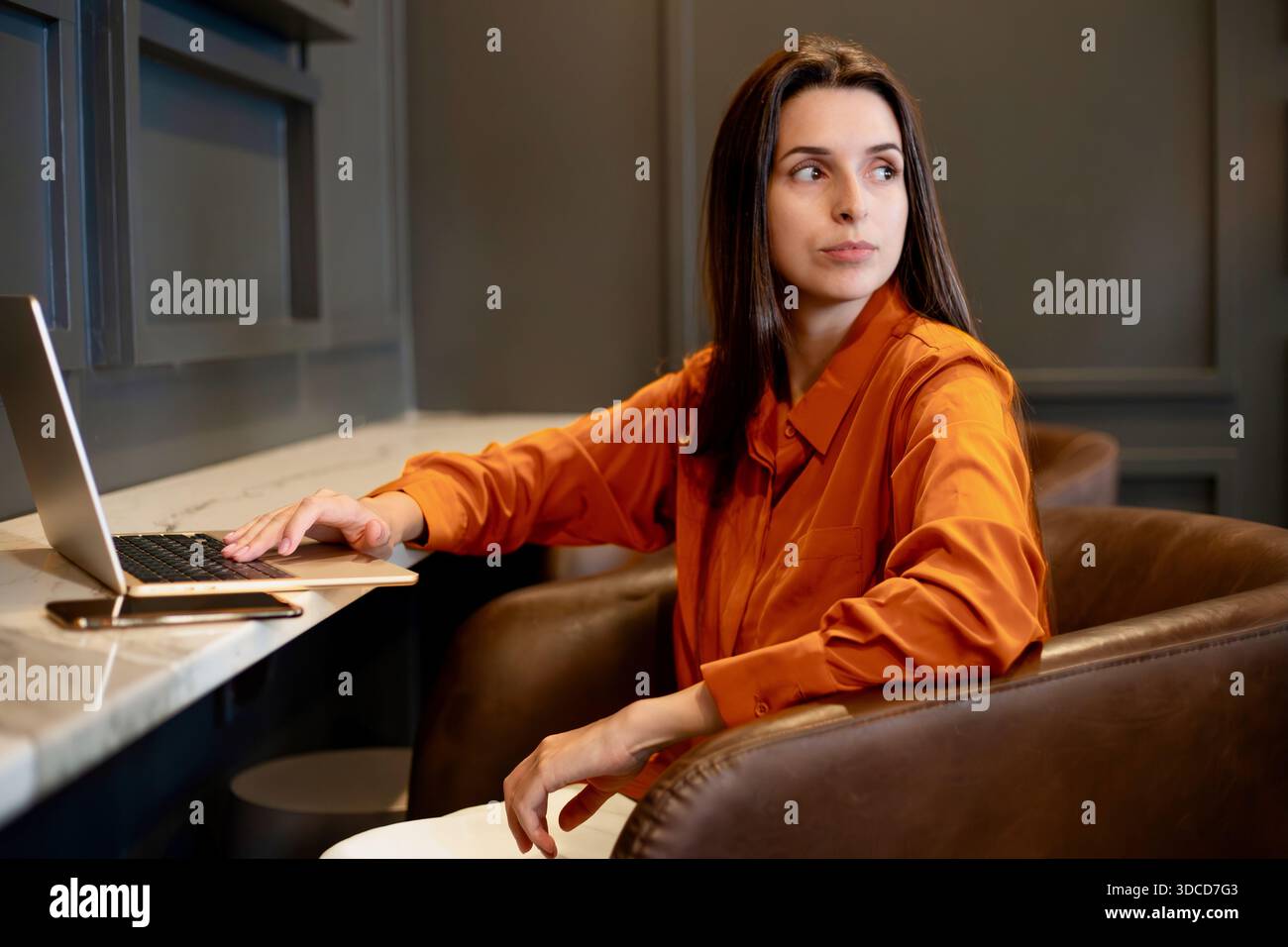 Professionelle Frau, die in einem modernen Innenarbeitsbereich mit einem Laptop sitzt und ein Geschäftsporträt, Fernarbeit und digitale Arbeitsabläufe in einem zeitgenössischen Format zeigt Stockfoto