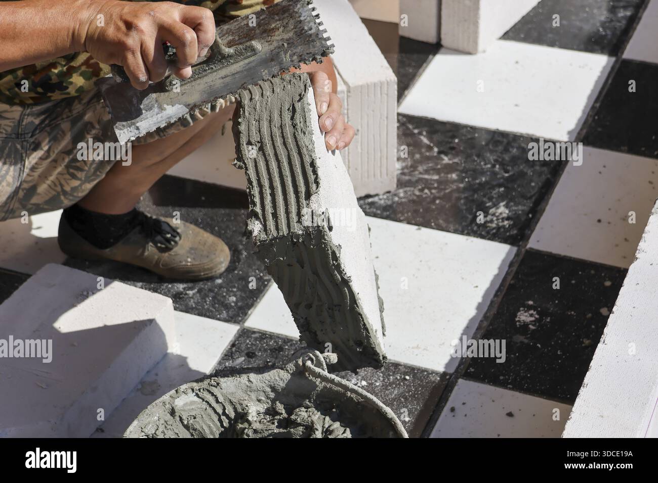 Konzentrierter Arbeiter, der Kleberzementmörtel auf Porenziegel aufträgt, indem er Kelle für Details zur Gebäudesanierung verwendet, die konzentrierten Anstrengungen demonstrieren Stockfoto