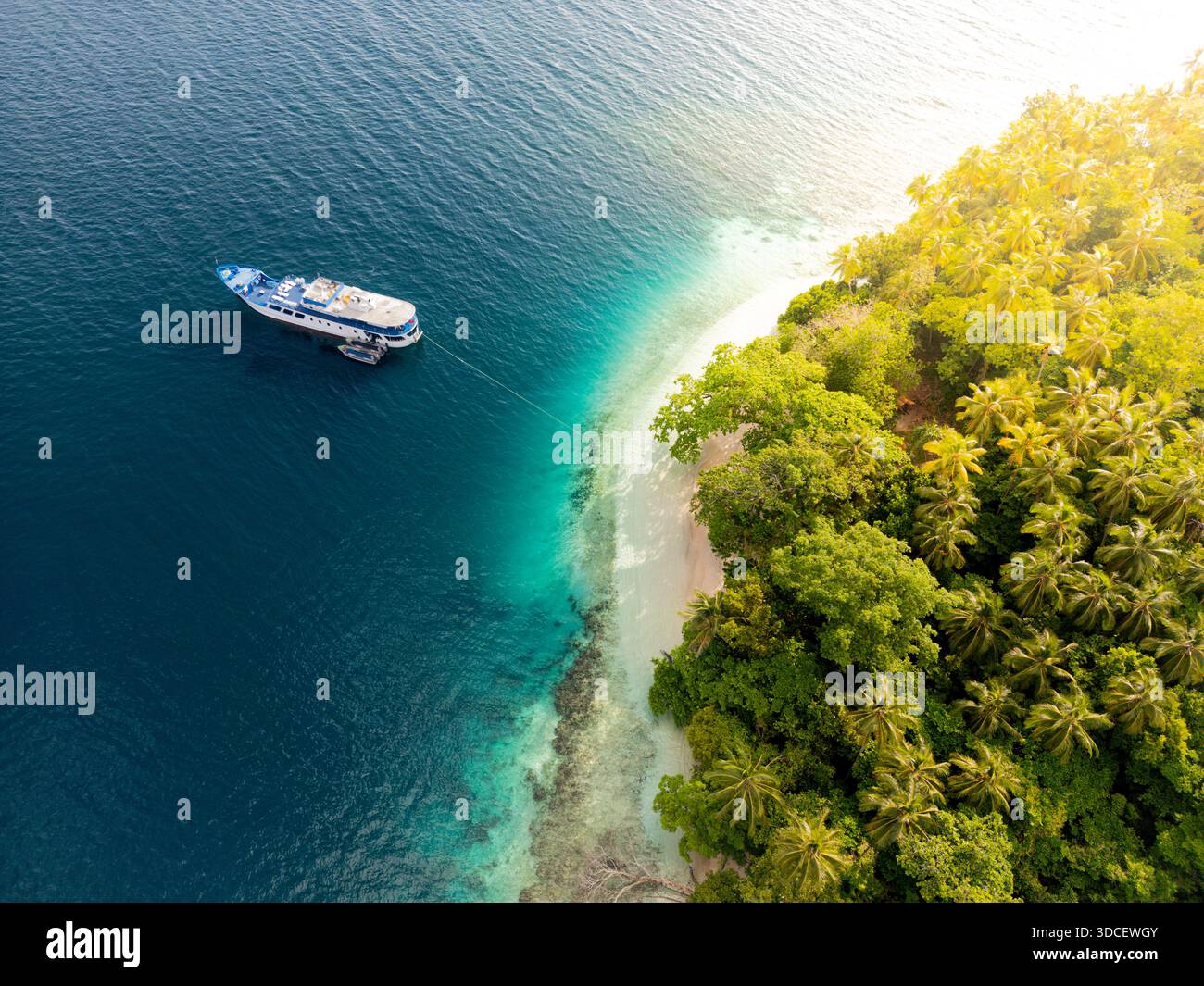 Blick aus der Vogelperspektive auf das Schiff, das von einer kleinen Insel mit goldenem Morgenlicht vertäut ist Stockfoto