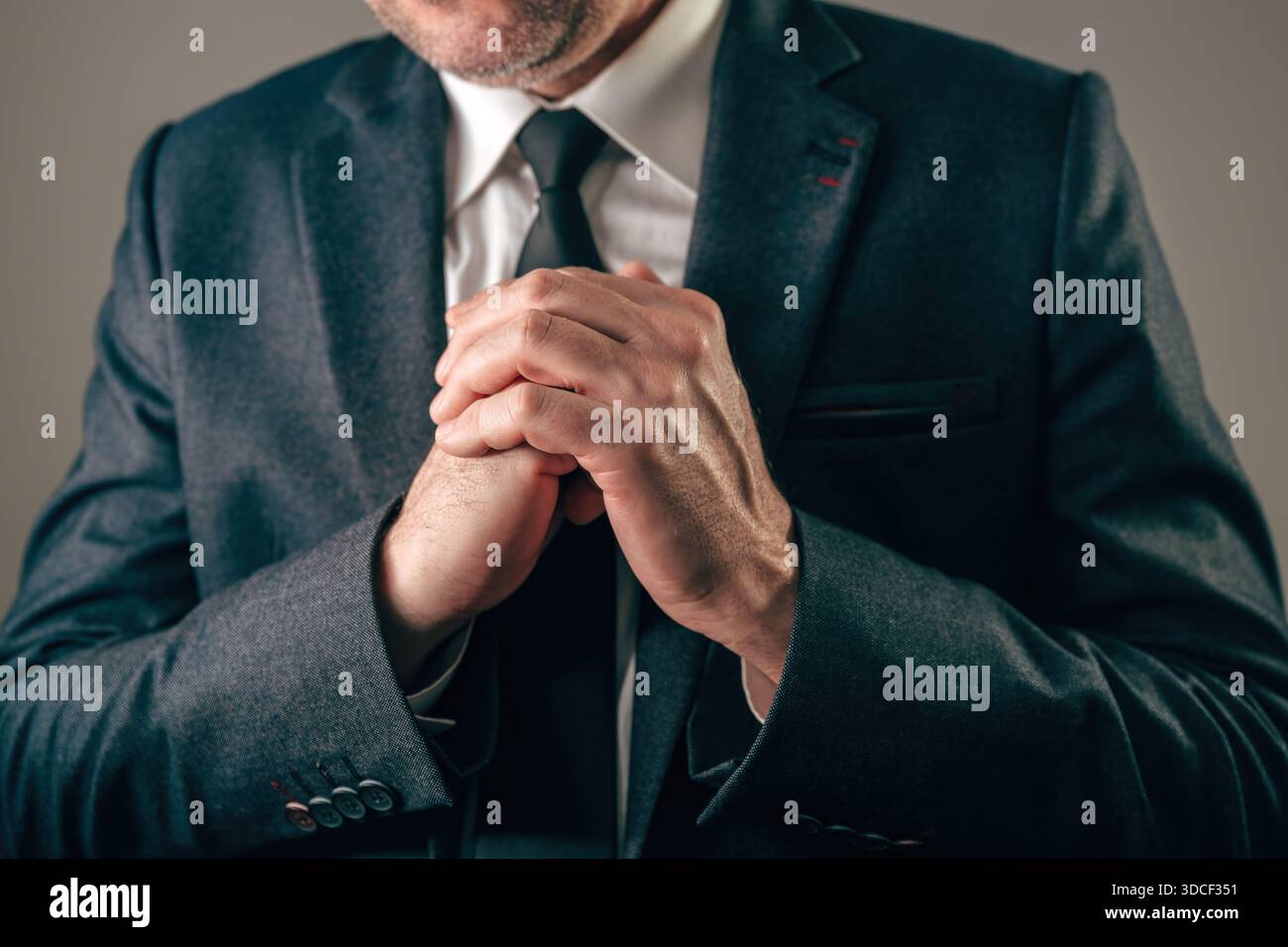 Geschäftsmann in dunklem Anzug mit fest zusammengeschlossenen Händen vor der Brust, die intensive Sorgen, Hoffnung, Gebet oder Verzweiflung vermitteln. Selektiv fo Stockfoto