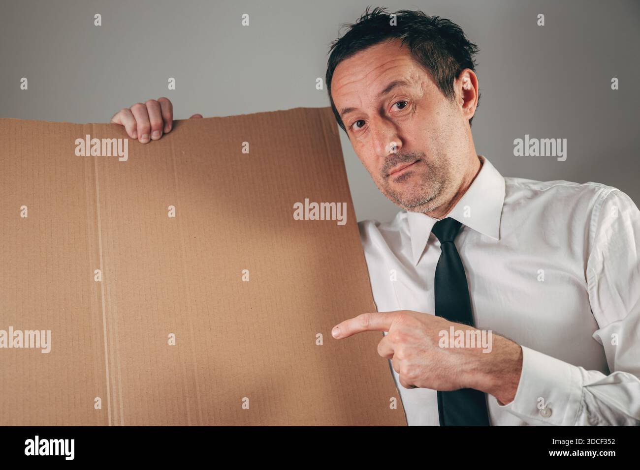 Geschäftsmann, der auf leere Pappe zeigt, Studio-Porträt mit Kopierraum, Präsentation, Ankündigung, Werbung, Botschaft, oder Kommunikationskonnektor Stockfoto