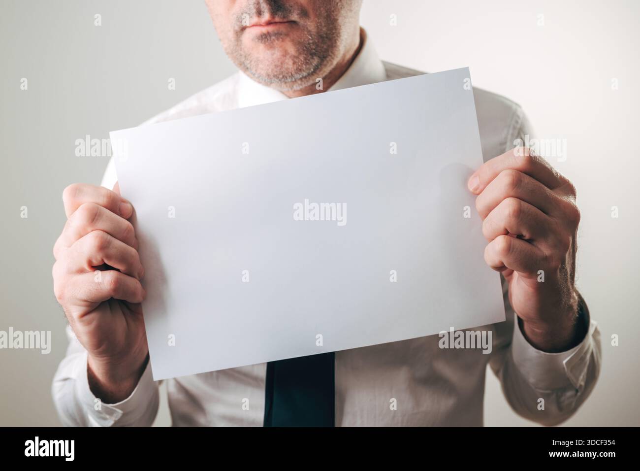 Seriöser Geschäftsmann, der im Büro ein leeres weißes Blatt-Modell hält, selektiver Fokus Stockfoto