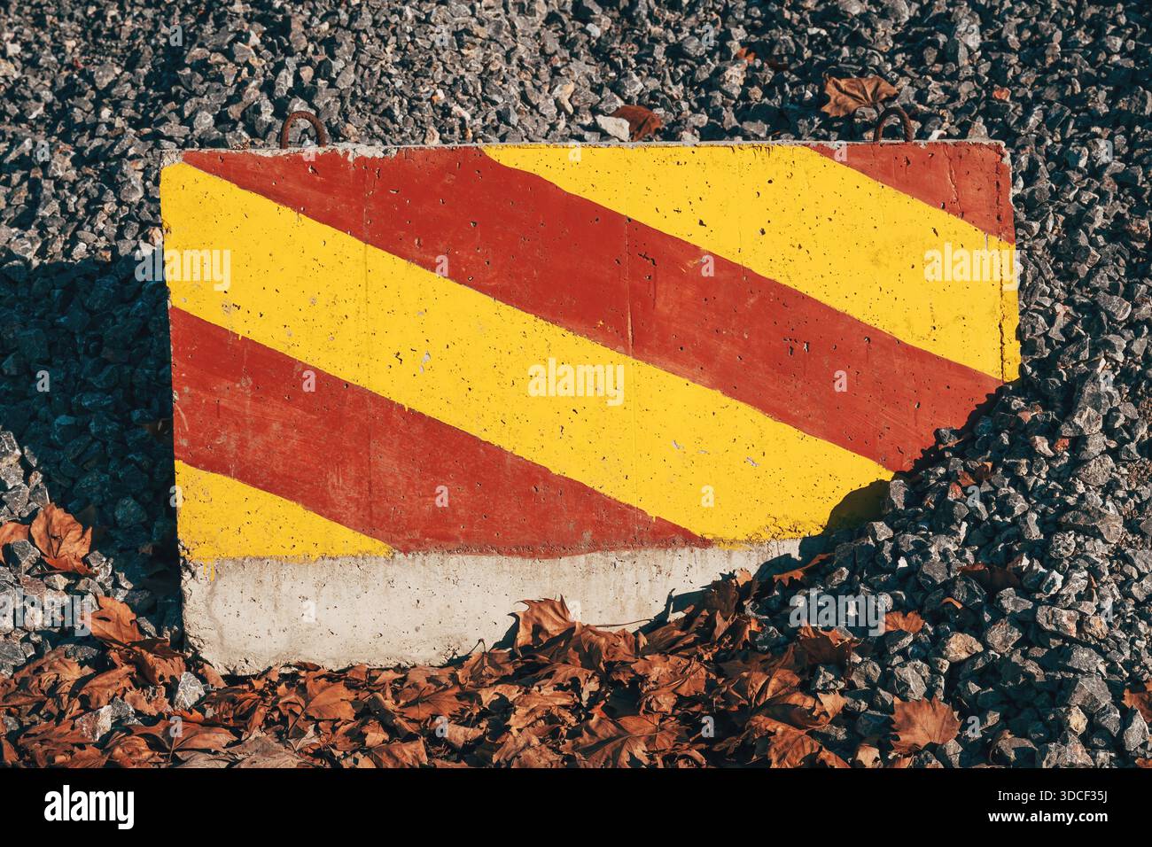 Betonbarriere mit gelbem und rotem Streifenmuster, die vor einem großen Schotterhaufen steht. Selektiver Fokus. Stockfoto