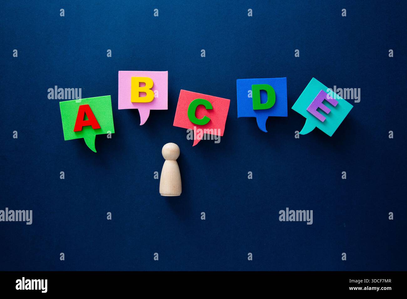 Holzfigur, die mit bunten Sprechblasen interagiert, die Buchstaben enthalten Stockfoto