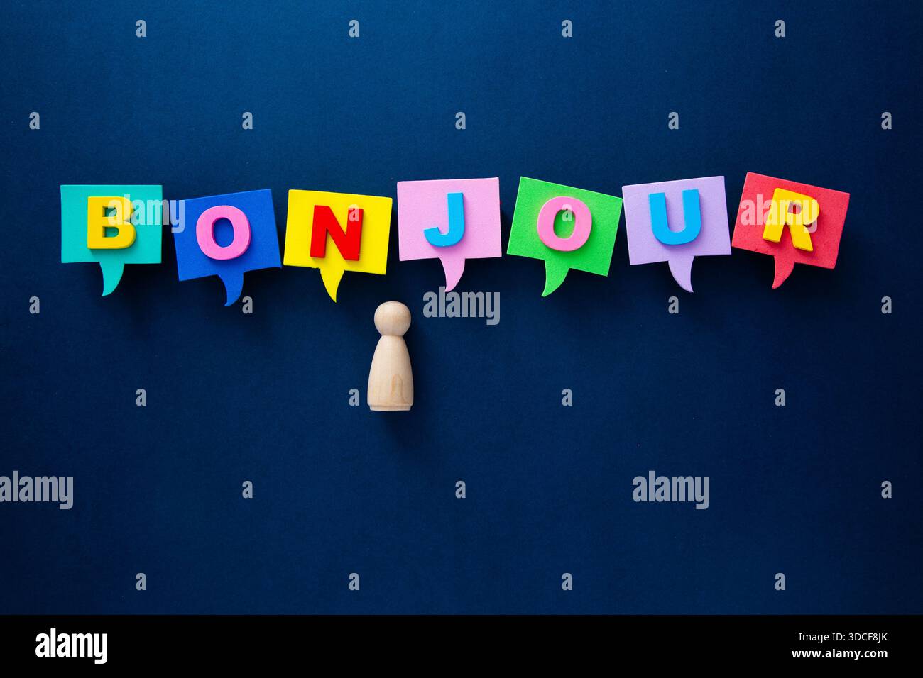 Holzfigur, die mit bunten Sprechblasen spielt, die bonjour auf einem dunkelblauen Hintergrund zeigen Stockfoto