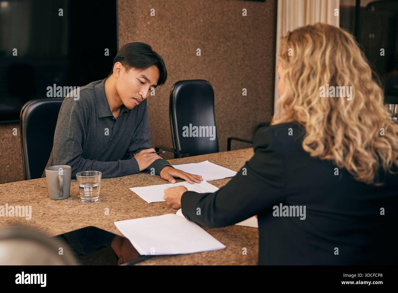 Mann, der sich die von einer Finanzberaterin erklärten Dokumente ansieht, während er in einer Kanzlei sitzt Stockfoto