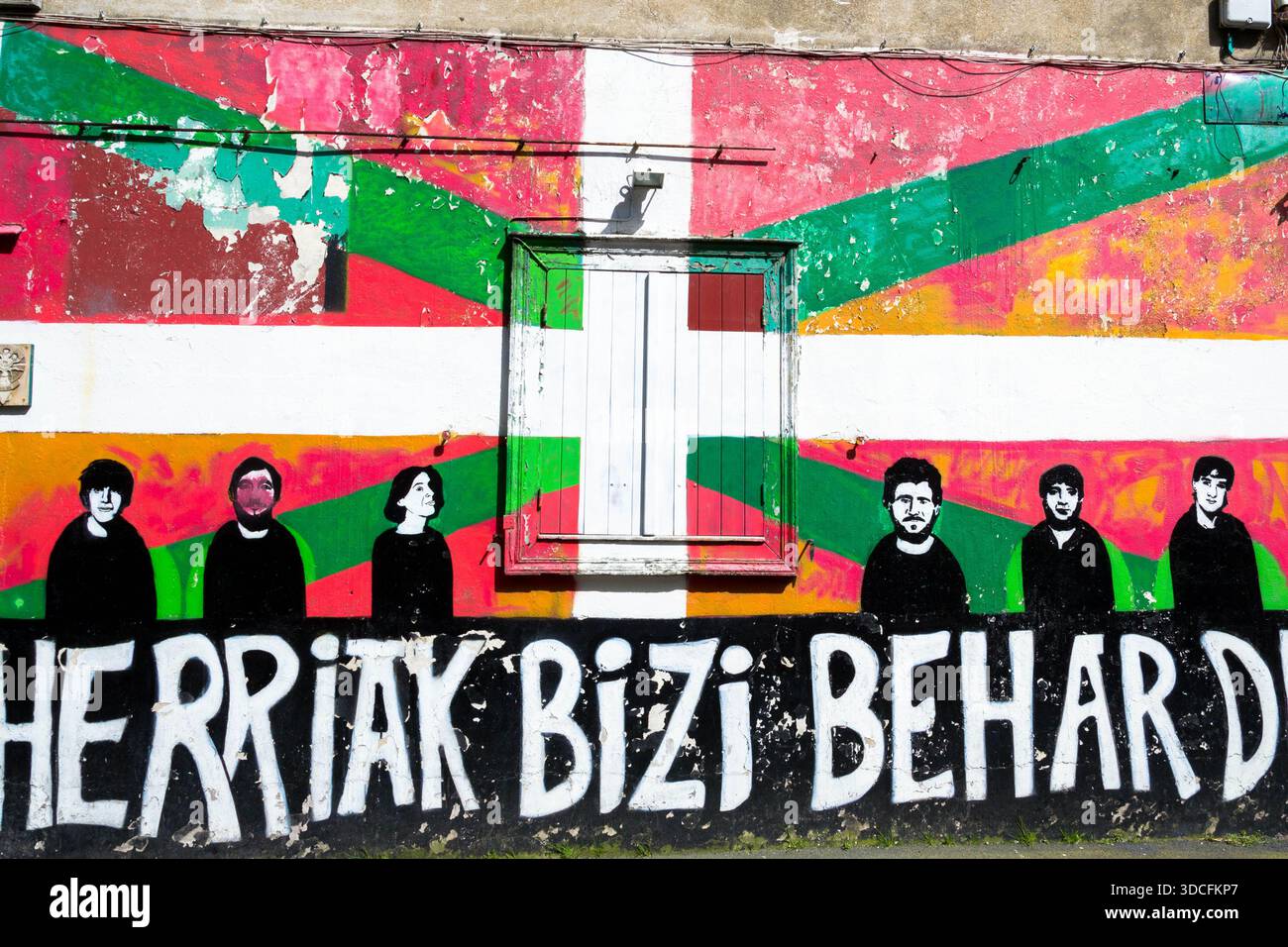 Blick auf ein markantes Wandbild mit der baskischen Flagge als Hintergrund und Silhouettenfiguren, leuchtende Farben kontrastieren alte Texturen der Wand, Bayonne, Frankreich Stockfoto