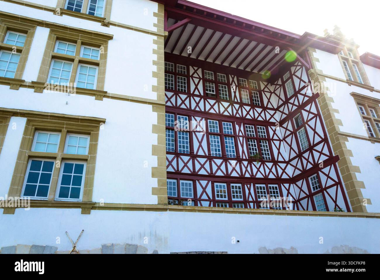 Blick auf das weiße Gebäude mit braunem Holzrahmen und Fensterreihen, die das Sonnenlicht reflektieren und eine faszinierende architektonische Szene schaffen. Stockfoto