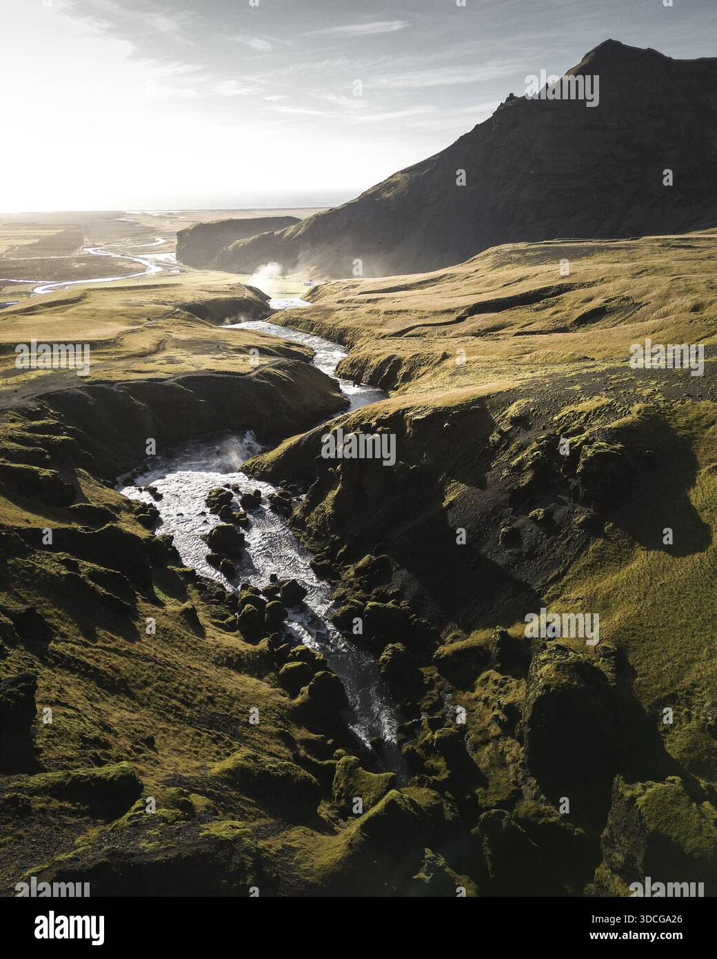 Aus der Vogelperspektive zieht sich ein mächtiger Fluss durch die moosige Landschaft in der Nähe von Vik, mit einem dunklen Berg im Hintergrund, Vik, westliche Region, Island Stockfoto