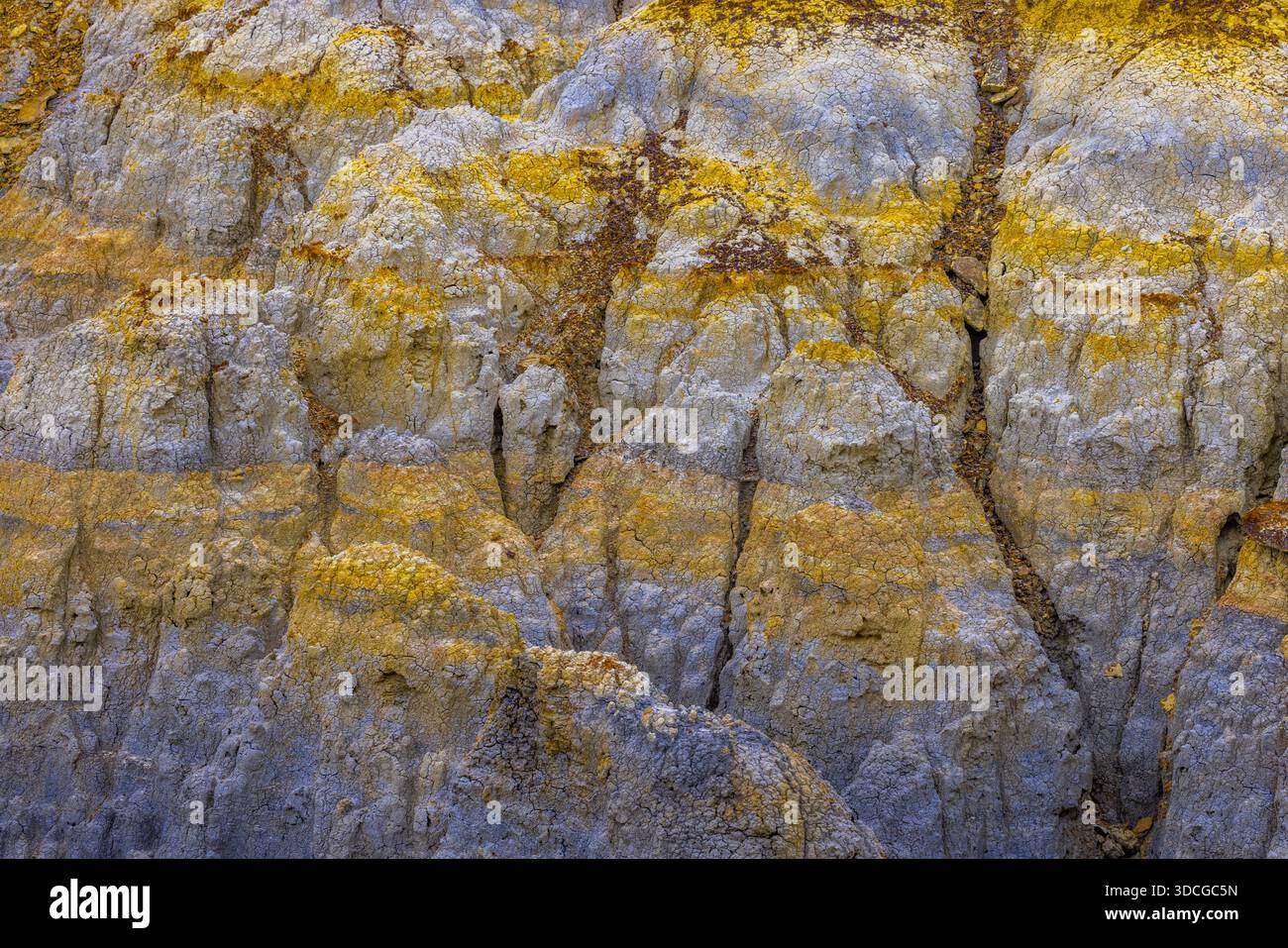 Blick auf zerklüftete, geschichtete Felsformationen mit leuchtenden gelben Streifen, die durch den grauen Stein schneiden und die Kunstfertigkeit der Natur, Shetpe, Mangystau Re, zeigen Stockfoto