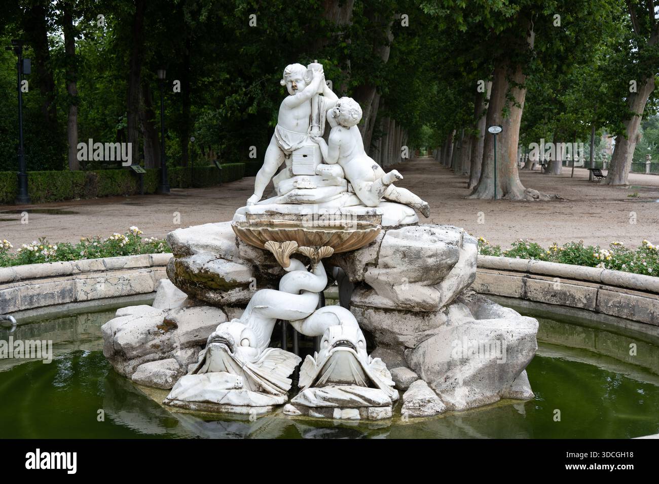 Ein dekorativer Brunnen mit Cherubiskulpturen, umgeben von Grün und einem Pfad Stockfoto