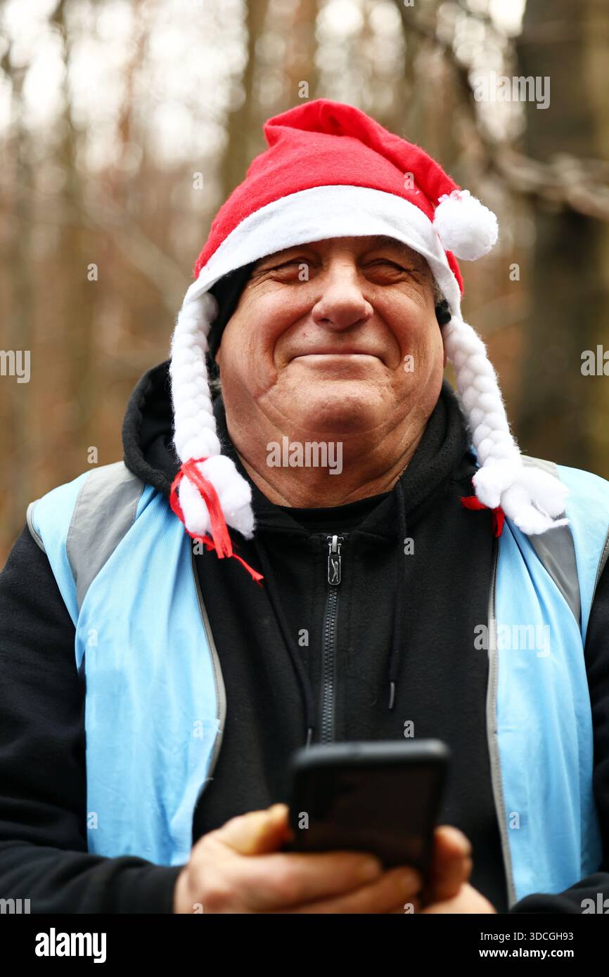 Ein lächelnder Mann im weihnachtsmann hält draußen ein Smartphone Stockfoto