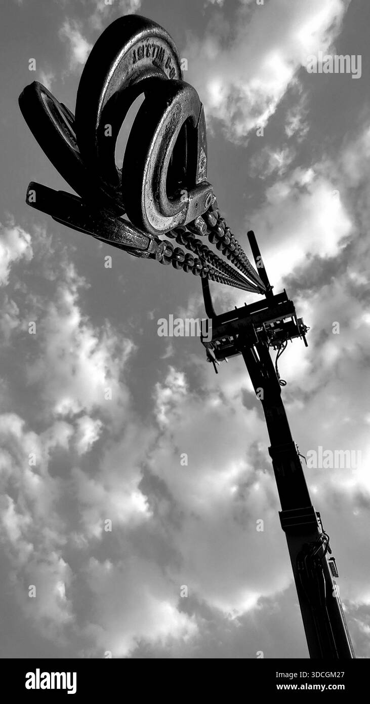 Schwarzweiß-Flachwinkelansicht eines Baukranauslegers mit schweren Stahlketten und Hubhaken, die in Richtung Himmel reichen. Dramatische Perspektive - Smartphone-aufgenommenes Stockfoto