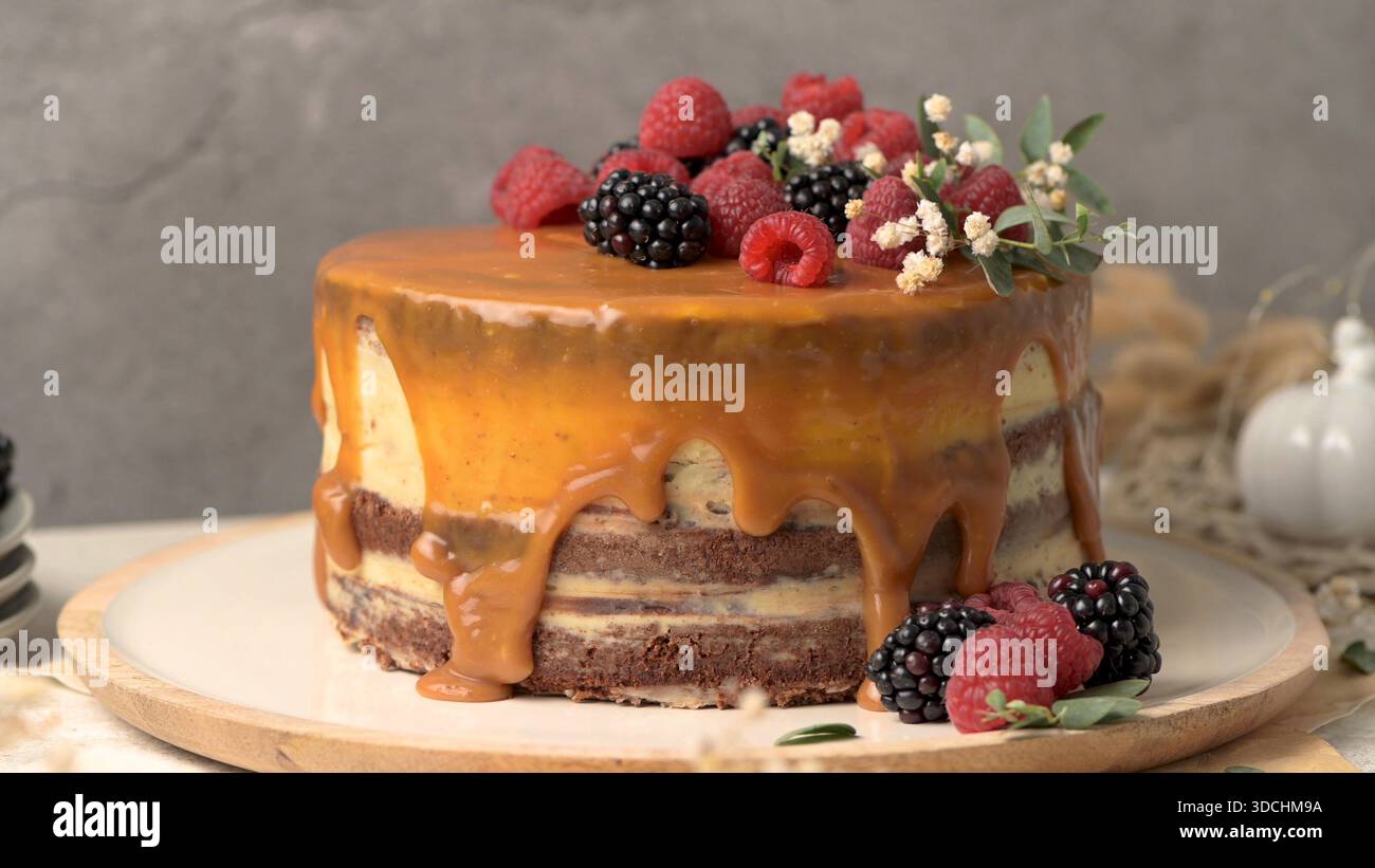 Ein dekadenter Schokoladen- und Vanillekuchen mit einer glänzenden Karamellglasur, die an den Seiten tropft. Frische Himbeeren und Brombeeren garnieren das Stockfoto