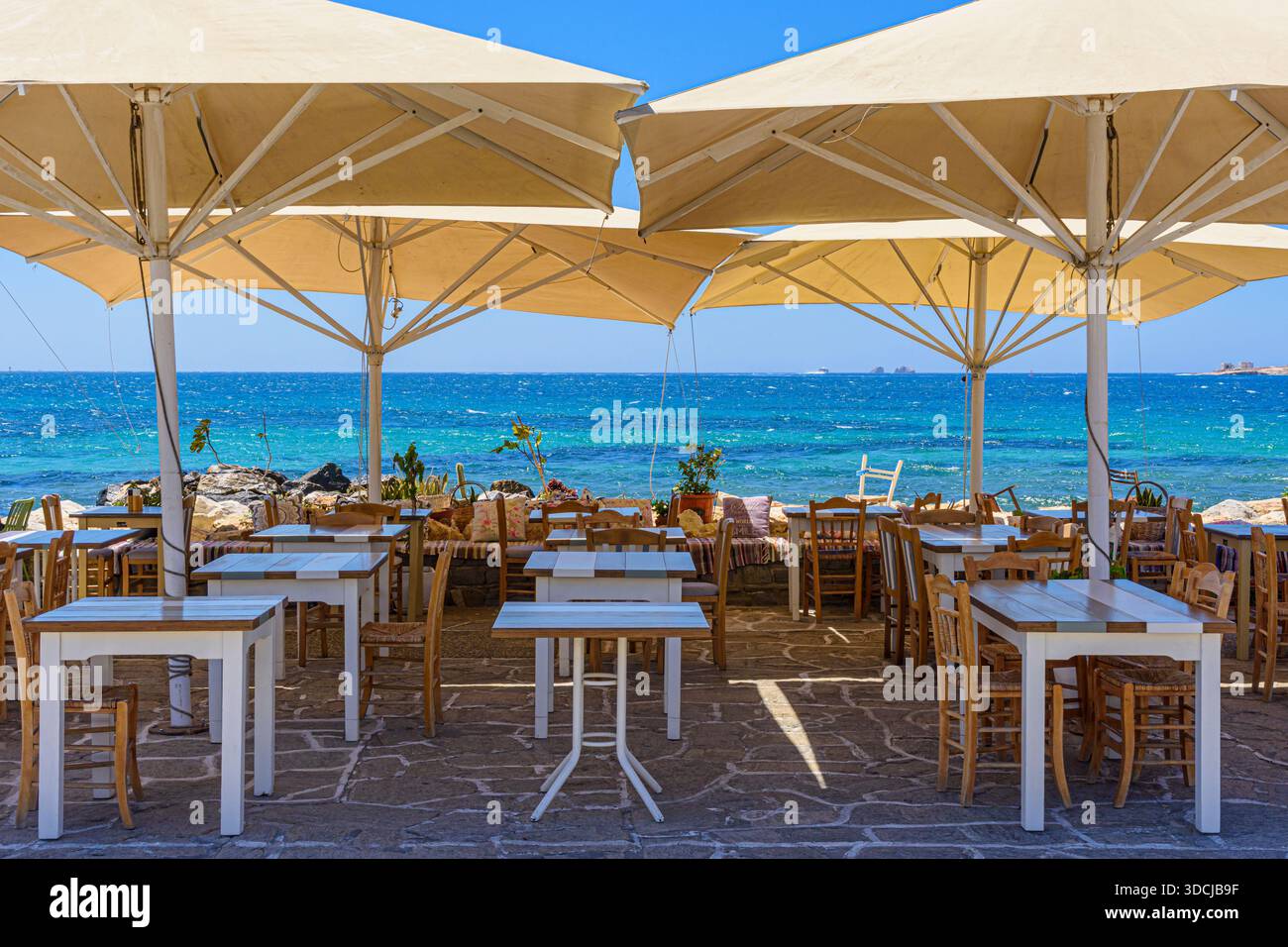 Tische und Stühle mit Sonnenschirmen entlang der Uferpromenade mit Blick auf die Bucht von Parikia, Parikia, Paros, Kykladen, Griechenland Stockfoto