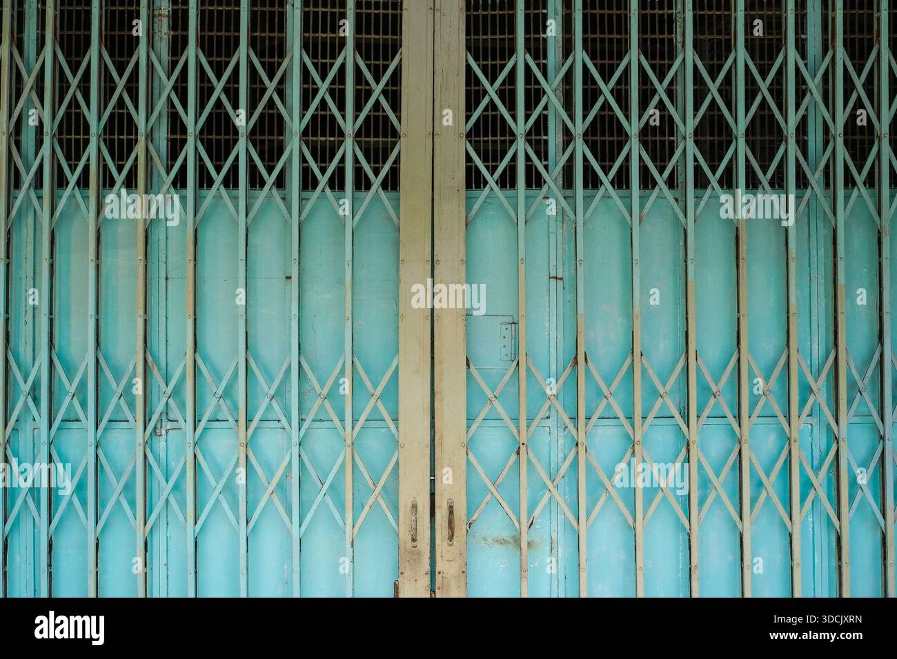 Symmetrisches türkisfarbenes, faltbares Metalltor mit diagonalem Gitterdesign an einer historischen Ladenfront in Malaysia. Stockfoto