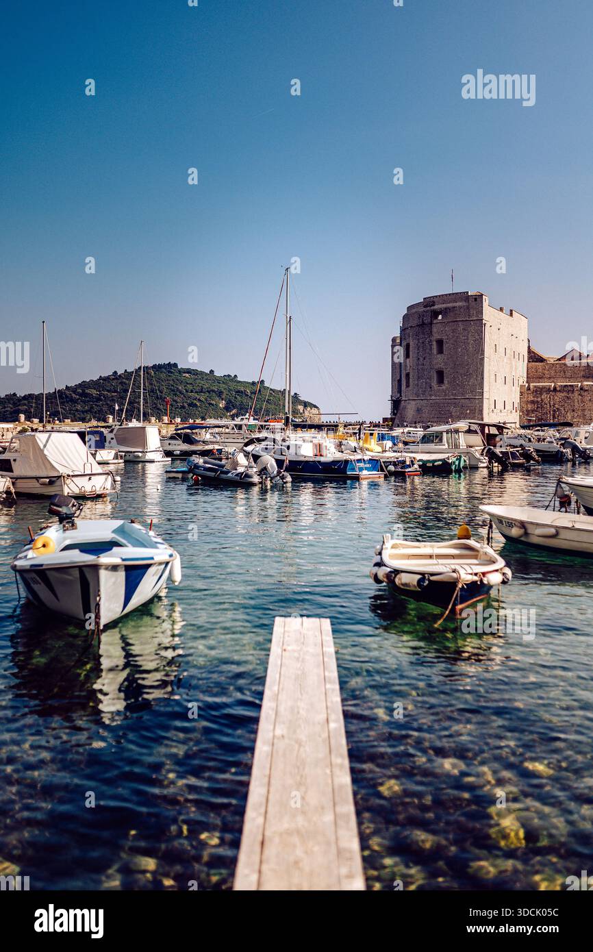 Blick auf Boote, die auf dem klaren Wasser schweben, mit der alten Steinfestung, die unter dem azurblauen Himmel bewacht wird, Dubrovnik, Dubrovnik-Neretva County, Cro Stockfoto