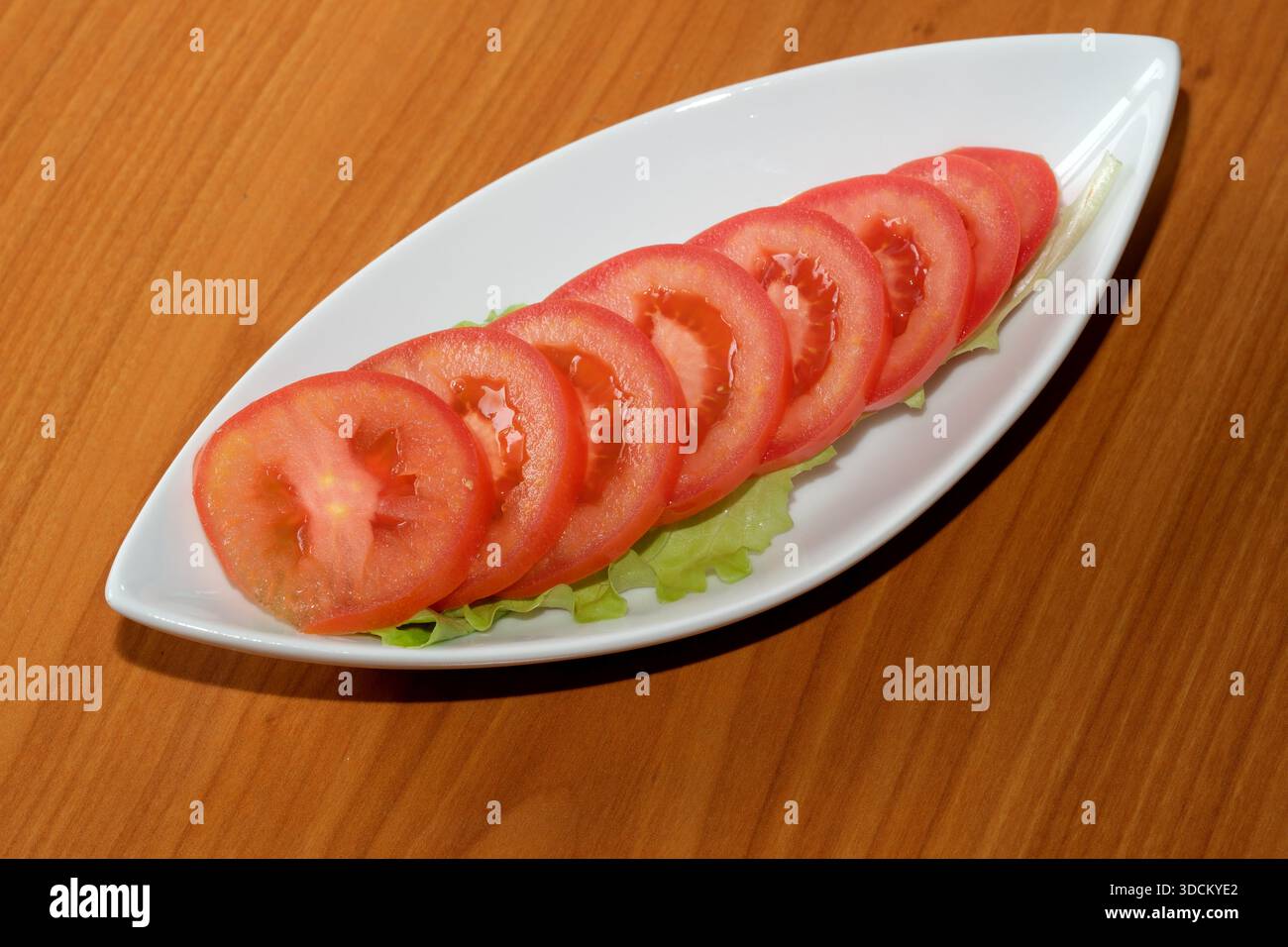 In Scheiben geschnittene Tomaten ruhen auf knusprigem Salat, der lebendige Farben und Frische bietet. Stockfoto