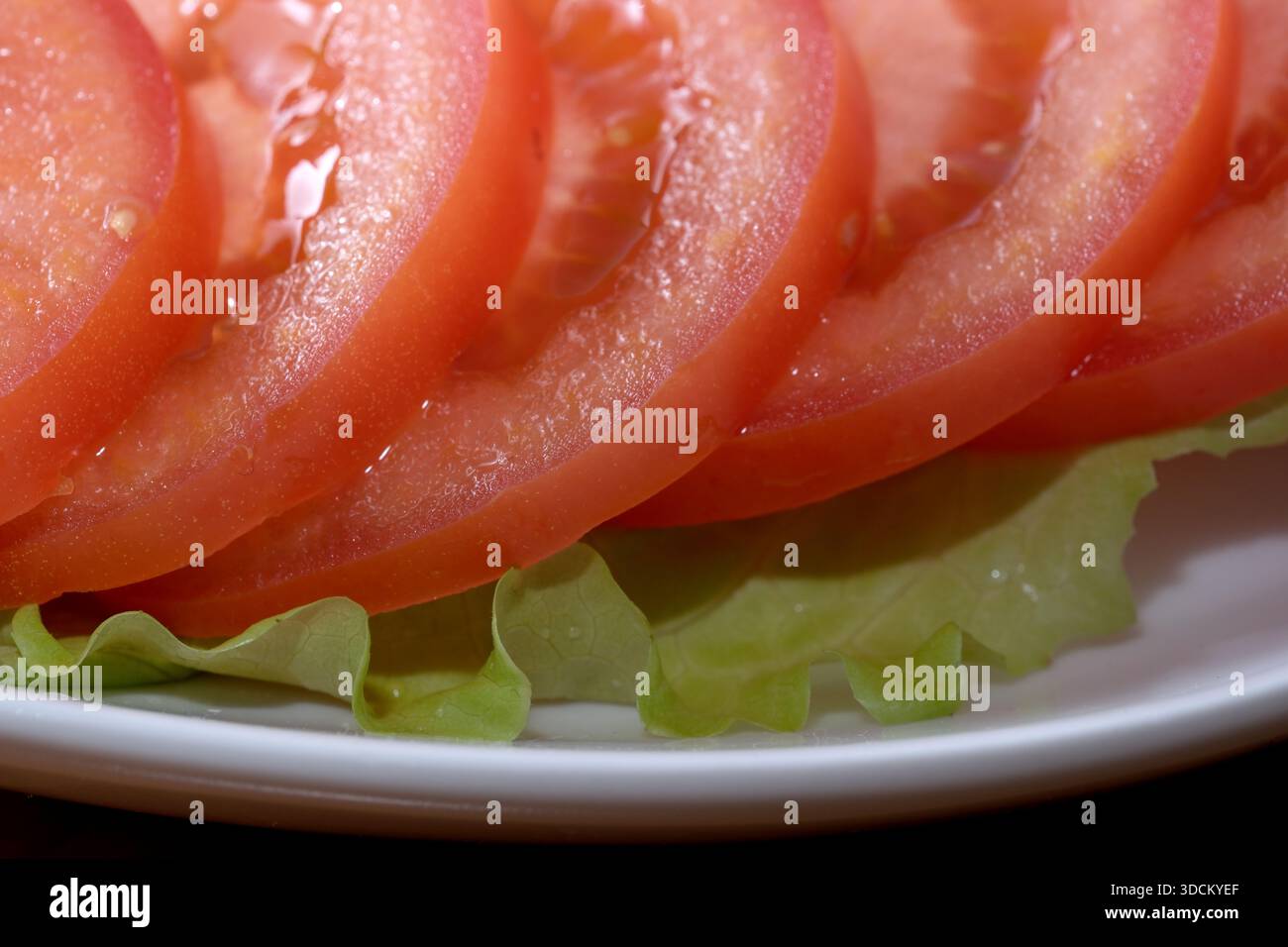 Hellrote Tomatenscheiben überlappen sich mit frischem grünen Salat und bilden so eine lebendige Teller. Stockfoto