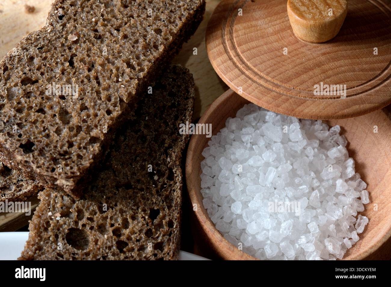 Frisch geschnittenes dunkles Brot ruht während des Mittagessens neben einer Schüssel mit grobem Salz. Stockfoto