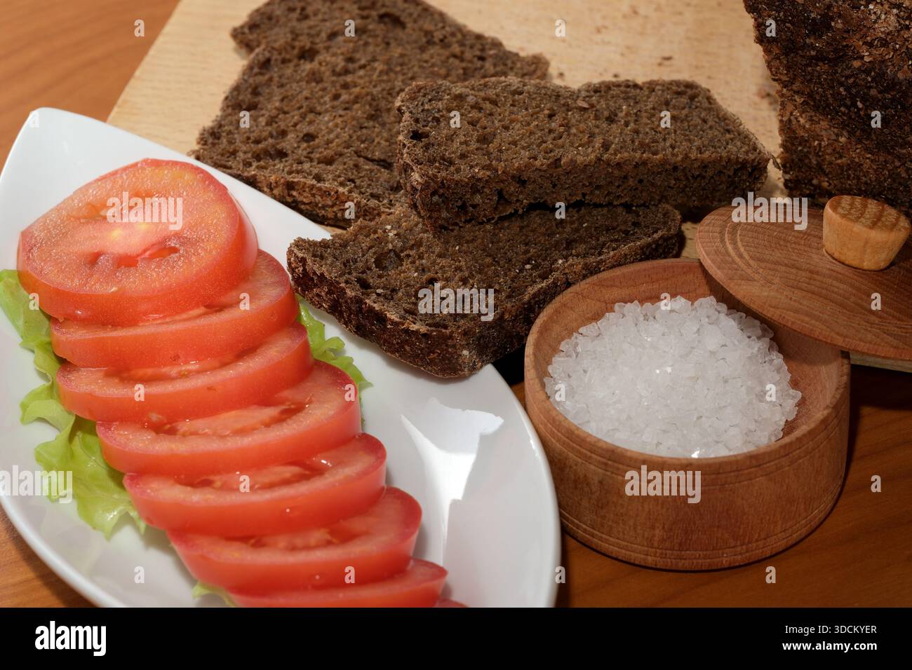Reife Tomatenscheiben und dunkles Brot zusammen mit grobem Meersalz sorgen für ein leckeres Gericht. Stockfoto