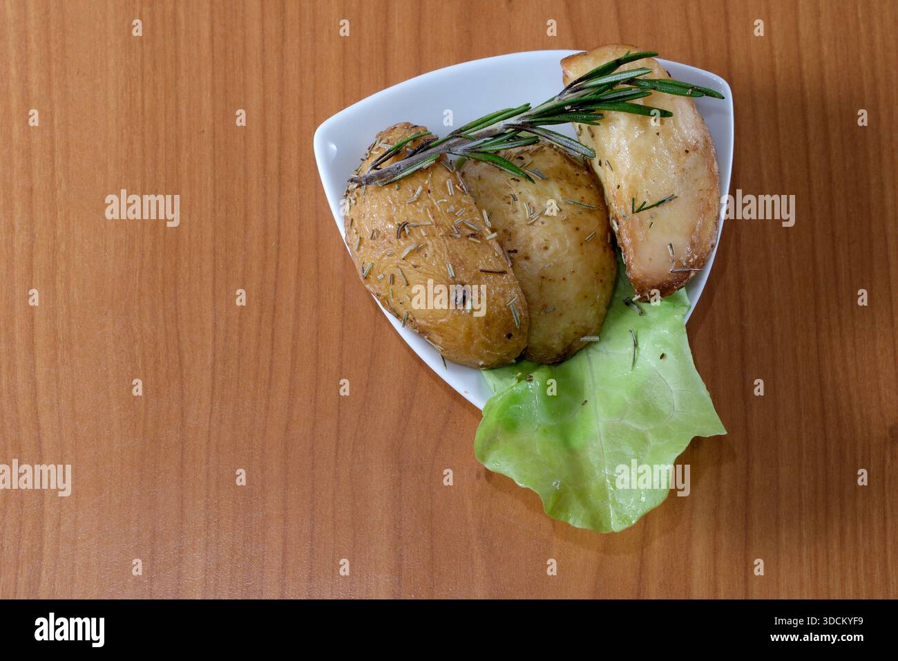 Goldbraune gebratene Kartoffeln, bestreut mit Rosmarin auf einem Teller mit Gemüse. Stockfoto