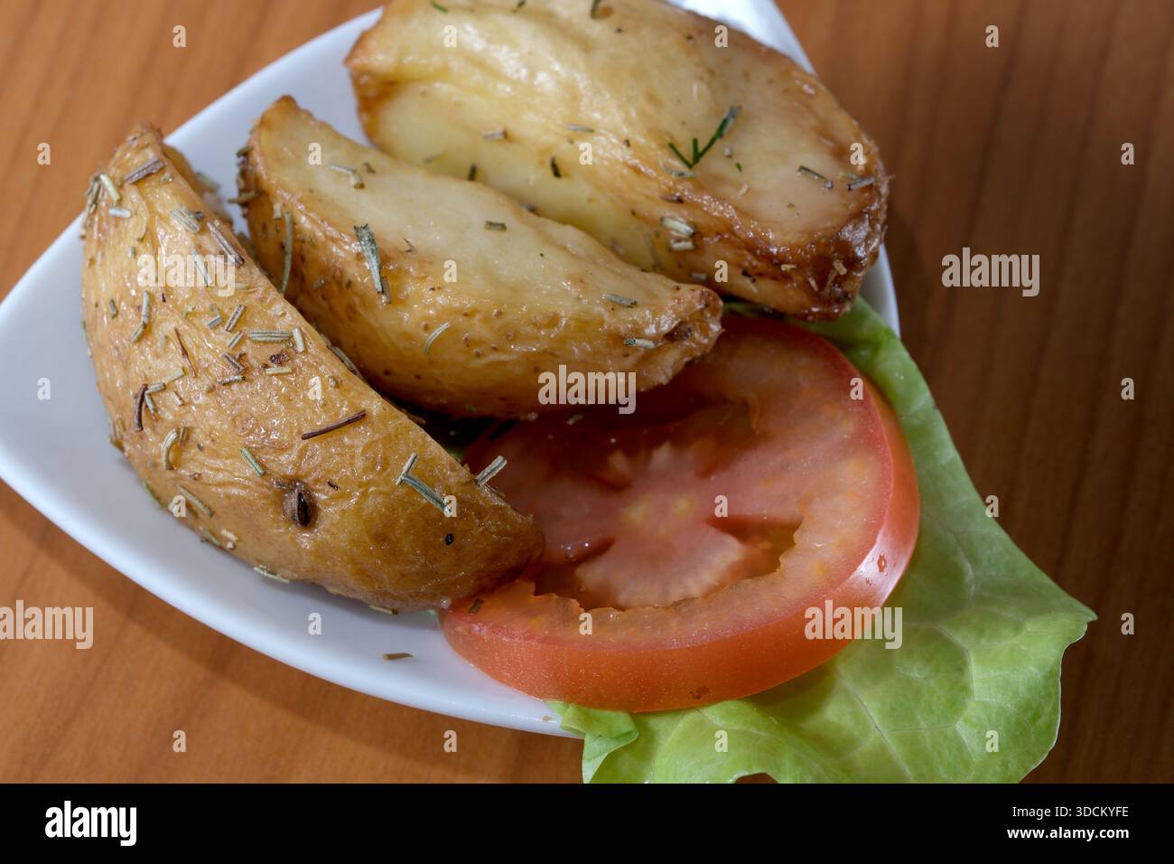 Herzhafte Kartoffelscheiben mit Kräutern sowie frische Tomatenscheiben und Salat. Stockfoto