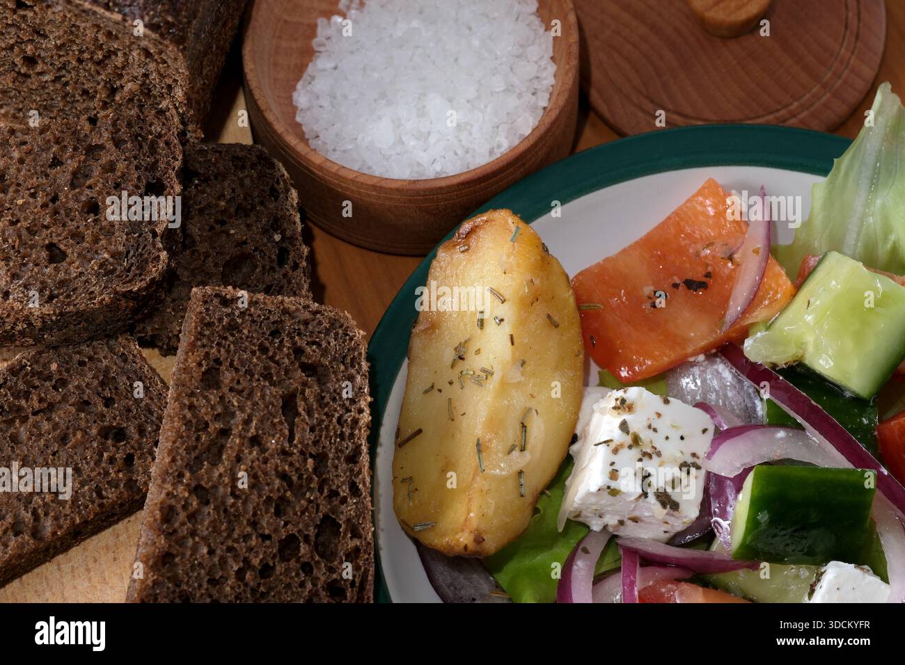 Farbenfroher Salat mit Tomaten, Gurken und Zwiebeln neben knusprigem dunklem Brot. Stockfoto
