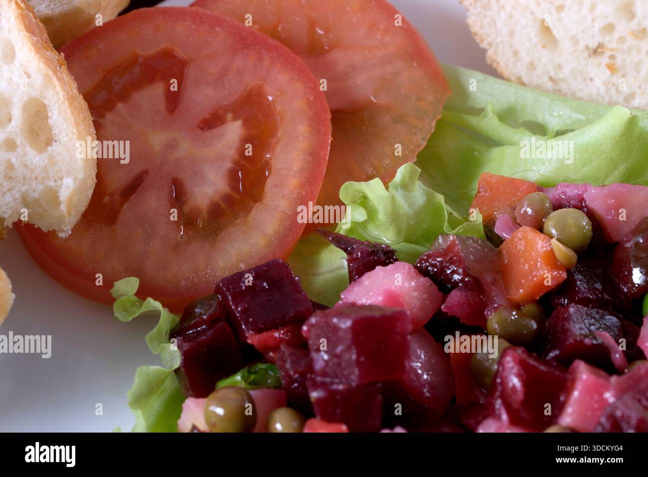 Farbenfroher Gemüsesalat begleitet von frischem Brot und Reifen Tomaten auf einem Teller. Stockfoto