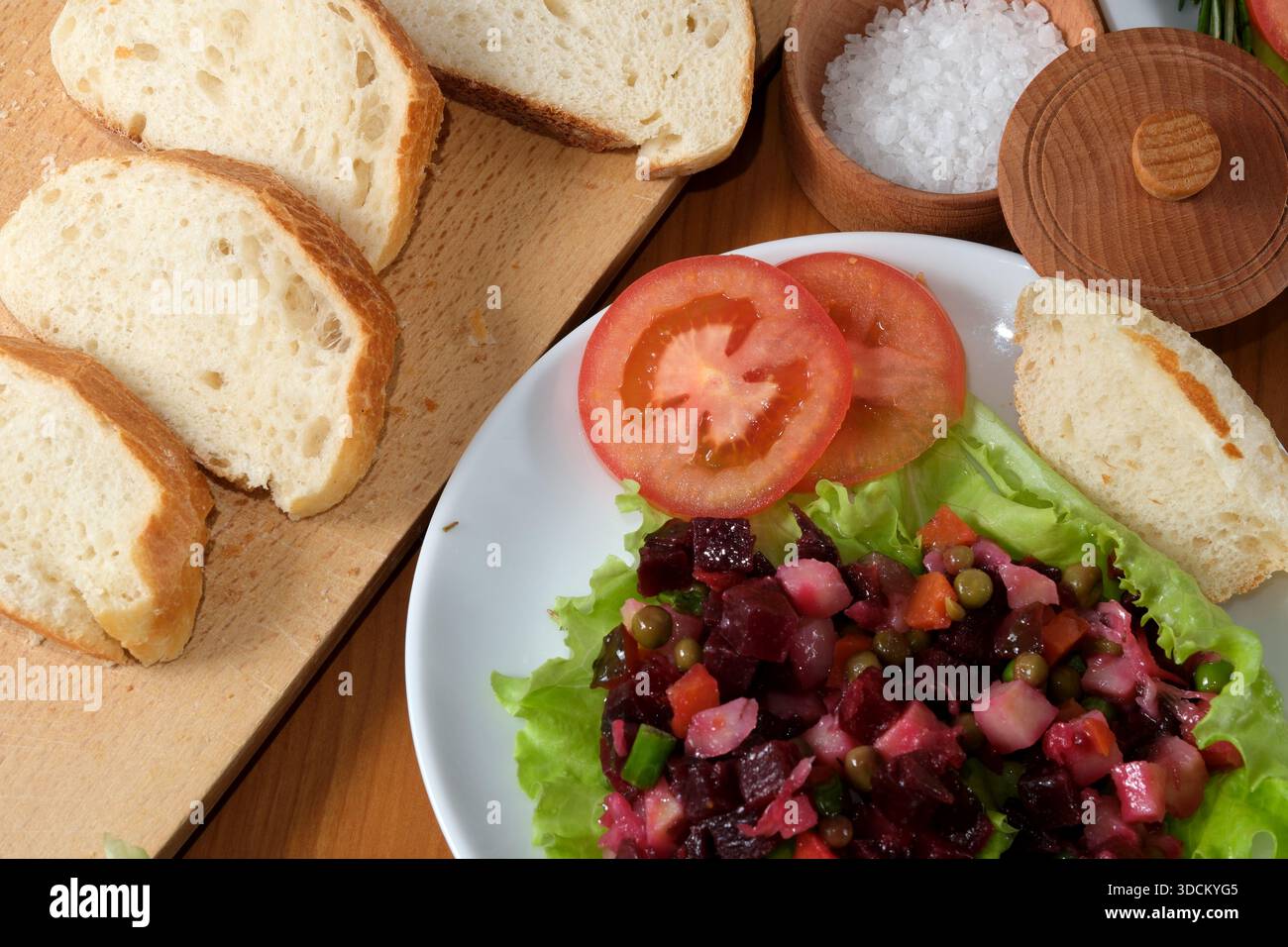 Farbenfroher Salat begleitet von frischem Brot und Gewürzen garniert auf einem rustikalen Tisch. Stockfoto