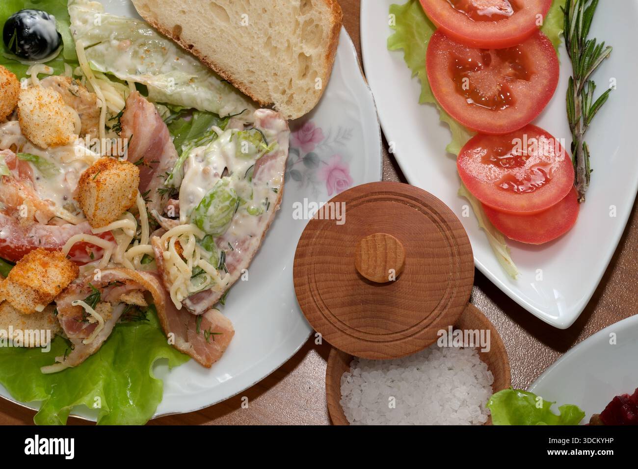 Leckerer Salat mit Gemüse, Croutons und einer Seite Tomaten auf Holztisch. Stockfoto