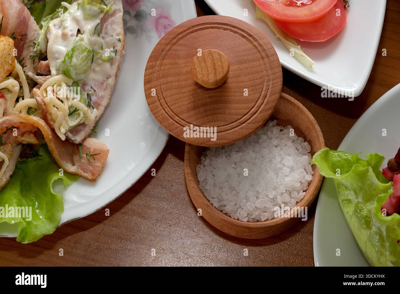 Eine kleine Schüssel Salz ergänzt eine bunte, frische Mahlzeit auf einem Holztisch. Stockfoto